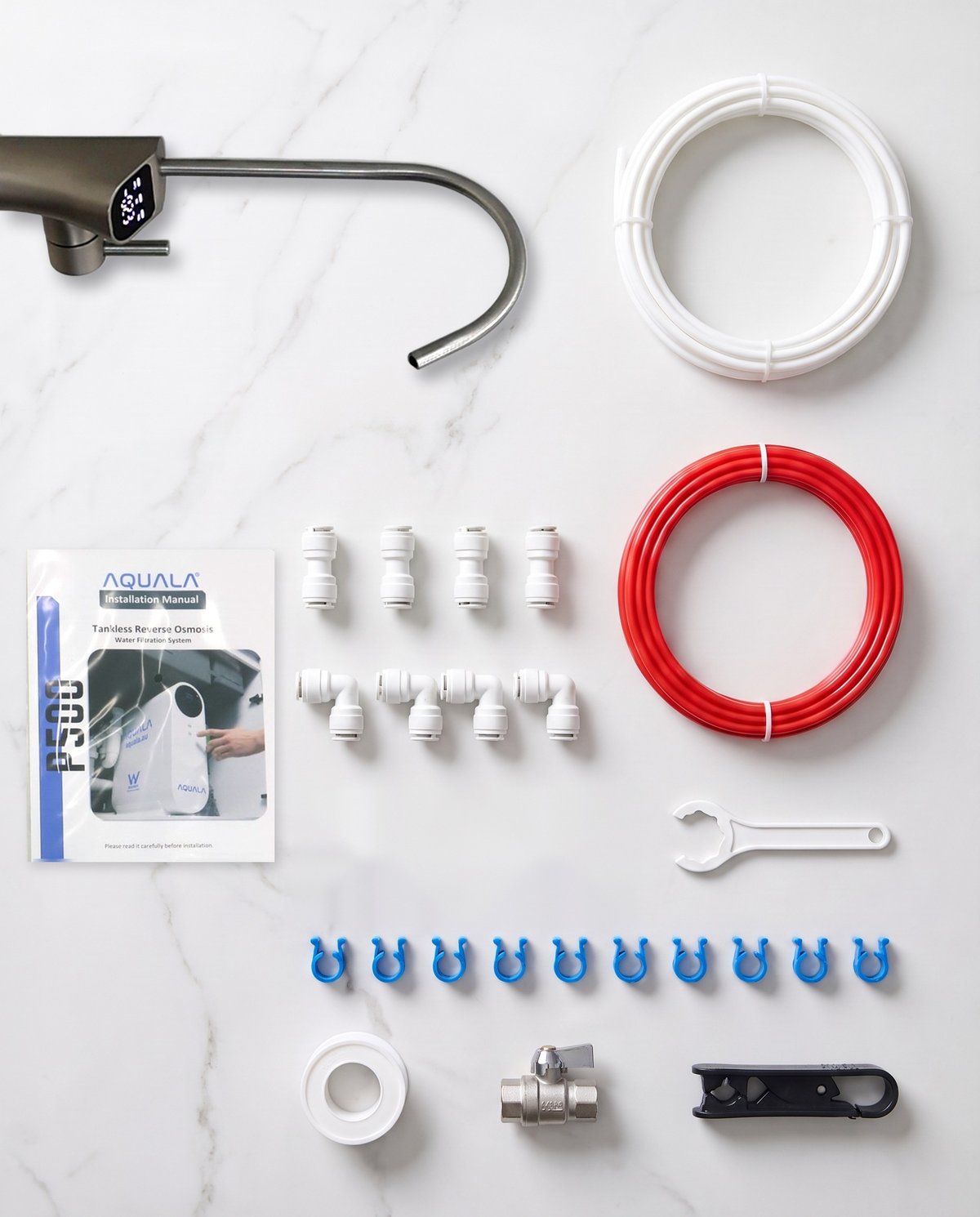 The parts in the box laid out on a marble bench: the filtered tap, a white tubing coil, the installation manual, push-fit fittings, a red tubing coil, a spanner, blue clips, thread tape, a valve and a tube cutter.